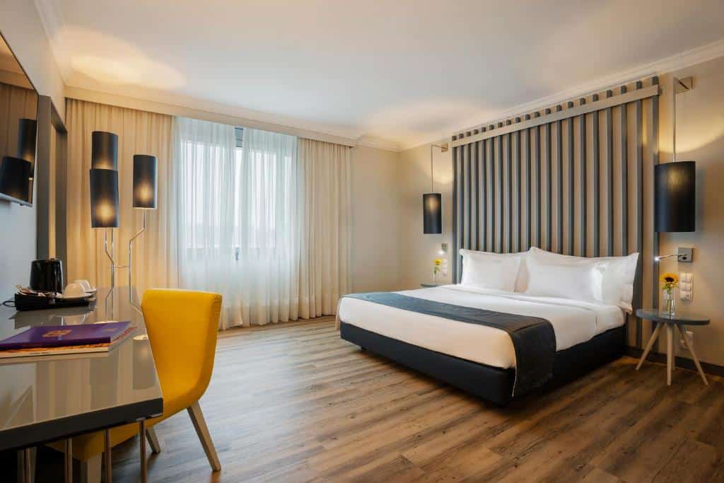 Quarto do HF Ipanema Park com cama de casal, mesinhas de cabeceira, uma mesa ampla com cadeira e televisão na parede.