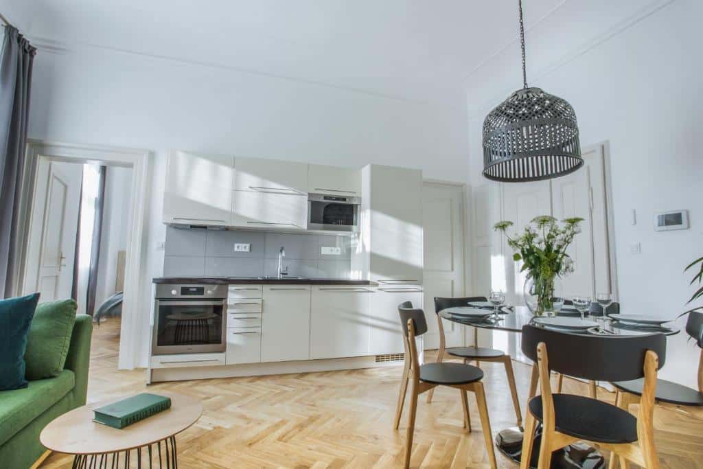 Cozinha moderna e zona de refeições do Lazenska N4 Residence, com armários brancos, mesa redonda, cadeiras de madeira e um sofá verde.