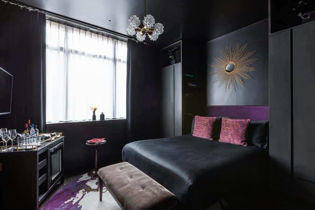 Quarto do The Mandrake todo em preto com detalhes em vinho, janela com cortinas, candeeiro de teto, televisão e um móvel de bar, com alcatifa em tons de roxo e branco
