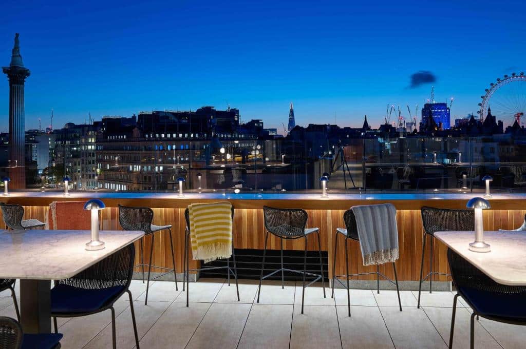 Terraço do The Trafalgar St. James com cadeiras com mantas, uma mesa com cadeiras e uma proteção de vidro com vista para a cidade.