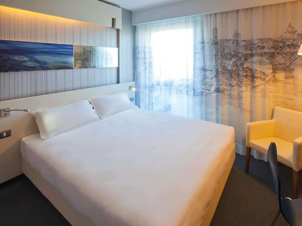 quarto do Ibis Styles Roma Eur, um dos hotéis baratos em Roma, com cama de casal grande, janela grande com cortinados decorados com árvores, cadeirão e candeeiro de ambos os lados da cama