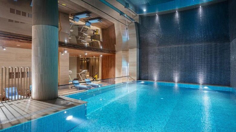 Piscina interior do Melas Hotel Istanbul com água azul, espreguiçadeiras, guarda-corpo de vidro e paredes modernas num ambiente de spa bem iluminado.