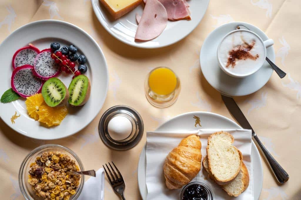 Pequeno-almoço no Hotel De la Paix, com pão, croissants, fruta, queijos e cappuccino.