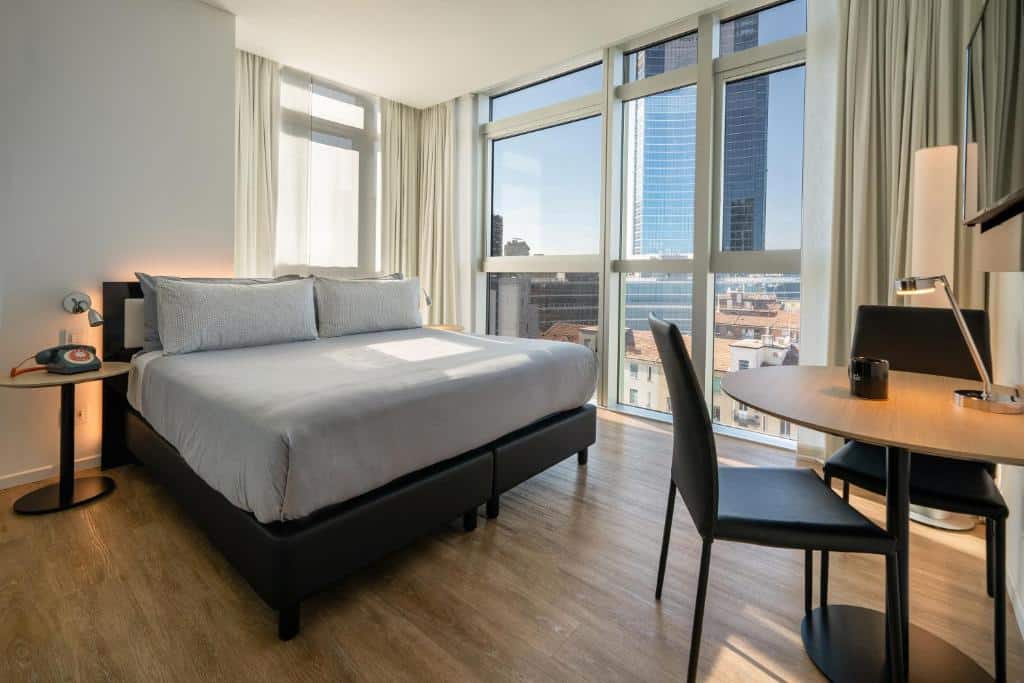 Quarto do INNSiDE by Meliá Milano Torre GalFa com uma janela panorâmica com vista para a cidade, uma cama de casal, uma televisão e uma mesa redonda com duas cadeiras