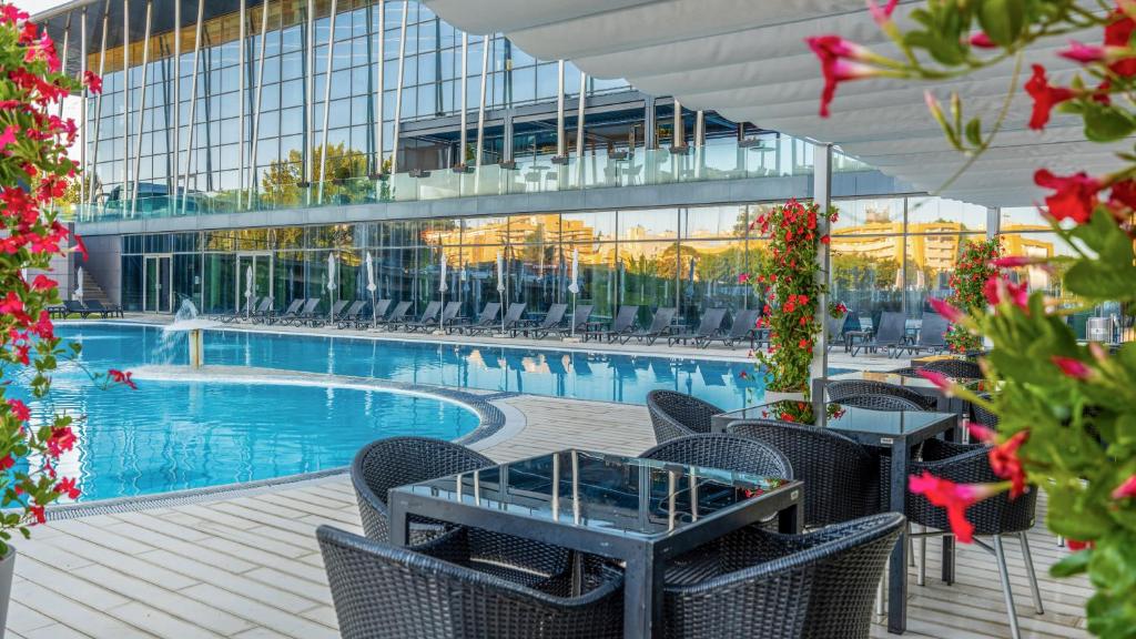 Zona da piscina exterior do Meliá Braga Hotel & Spa, com espreguiçadeiras, mesas de tampo de vidro e plantas, junto a um edifício de vidro.