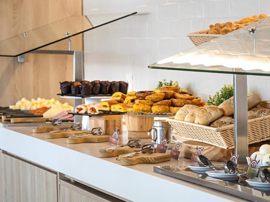 Pequeno-almoço servido num balcão do Ibis Styles Lisboa Centro Liberdade NE, com muito pão, pastéis de Belém, bolos e charcutaria à disposição