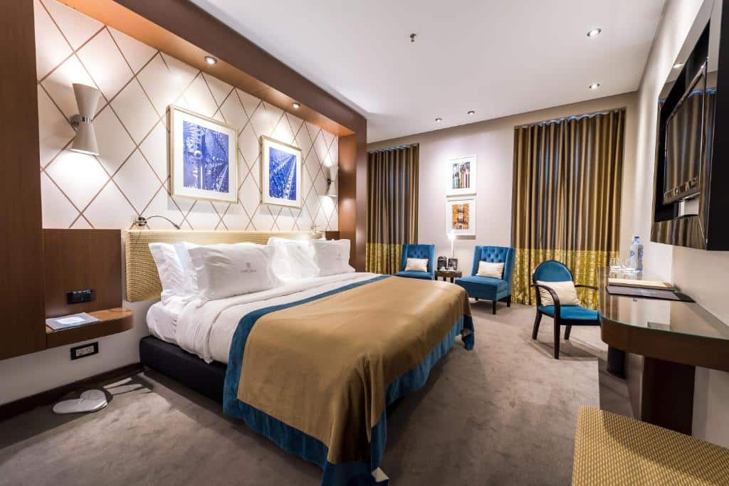 Quarto moderno no Lisboa Carmo Hotel com uma cama grande, duas cadeiras, uma secretária e arte na parede, em tons neutros e azuis.