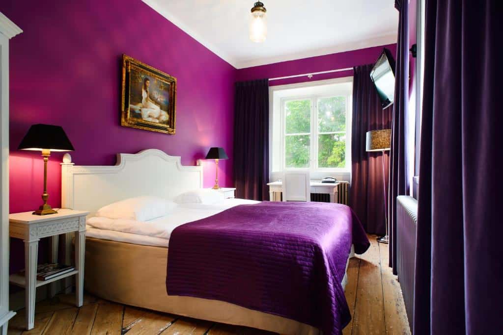 Quarto do Hotel Hellstens Malmgård com cama de casal e cómodas com candeeiros.