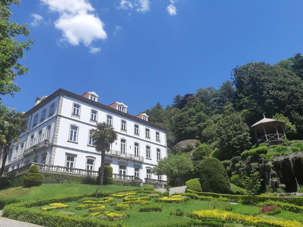 Grande edifício branco do Hotel do Parque, junto a jardins bem cuidados e a um coreto de madeira, sob céu azul.