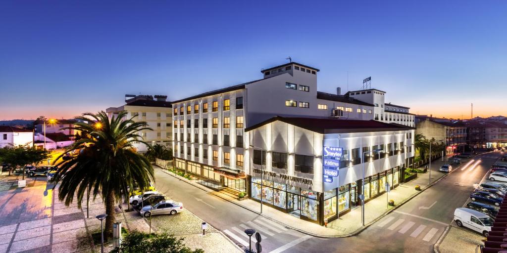 O Steyler Fátima Hotel Congress & Spa, com vários andares e uma grande placa na esquina, num cruzamento com carros estacionados e palmeiras ao anoitecer.
