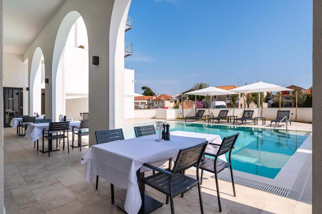 Restaurante com mesas ao lado de piscina numa área exterior ensolarada, no Miramare Hotel, em Kolovare