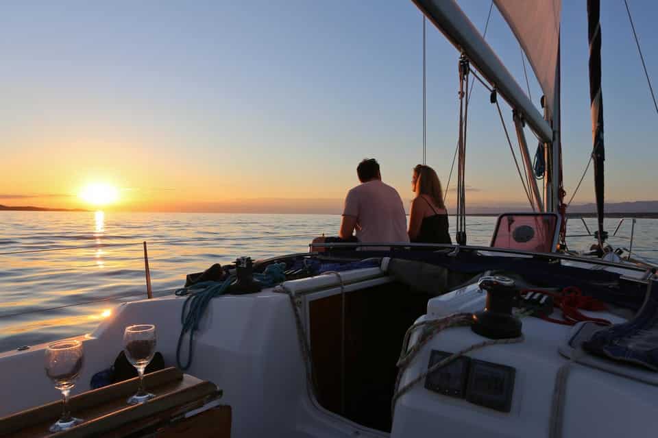 Um casal sentado num veleiro a observar o pôr do sol sobre as águas calmas de Hvar, com duas taças de vinho numa mesa ao lado.
