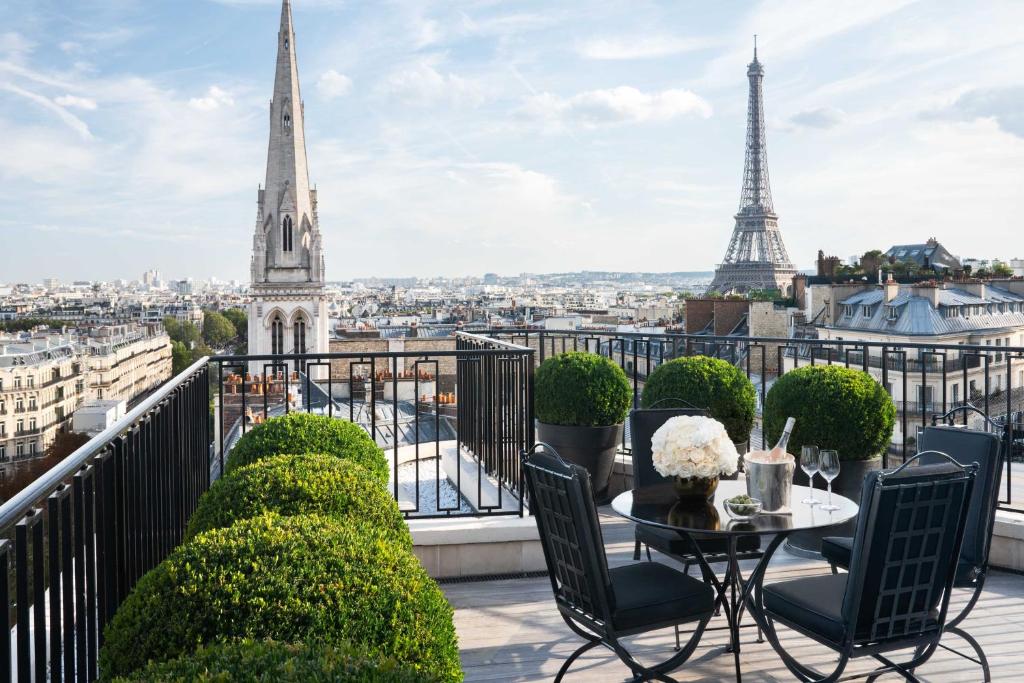 Um terraço na cobertura do Four Seasons Hotel George V Paris com uma mesa, cadeiras, plantas e vista para os pontos de referência de Paris, incluindo a Torre Eiffel e a torre de uma igreja. Este é um dos hotéis de luxo em Paris.