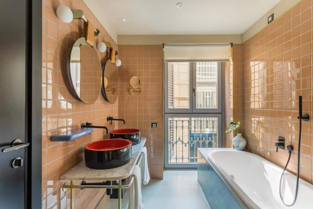 Casa de banho do Room Mate Giulia com banheira de hidromassagem junto a uma janela, móvel com duas bacias redondas e dois espelhos redondos