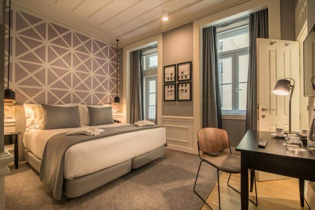 Quarto acolhedor no Hotel da Baixa, com cama de casal, candeeiros suspensos sobre as mesas de cabeceira, janelas com cortinas blackout e secretária com TV na parede.