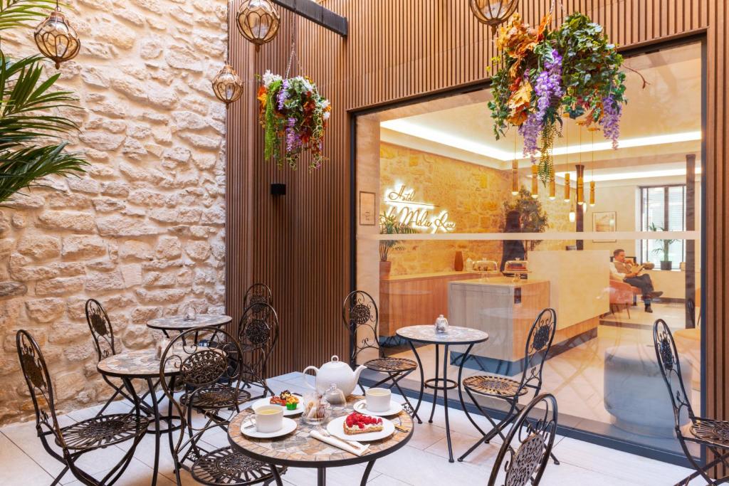 Pequeno pátio exterior do Hôtel Le Milie Rose com cadeiras de metal preto, mesas de mármore e plantas suspensas.