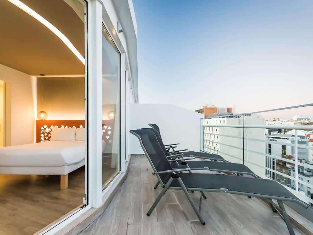Varanda do Ibis Styles Lisboa Centro Marquês de Pombal com quatro poltronas pretas e vista para a paisagem urbana.