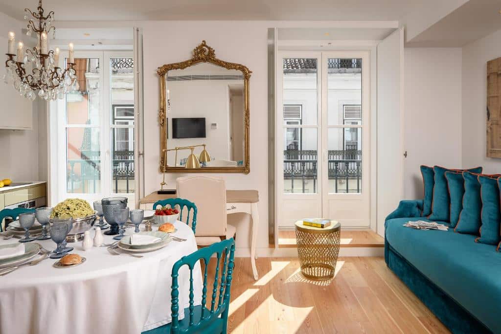Sala de estar do Residentas Aurea com duas varandas, uma mesa posta com itens de café, cadeiras azuis e um sofá da mesma cor, além de um lustre e um espelho de estilo colonial