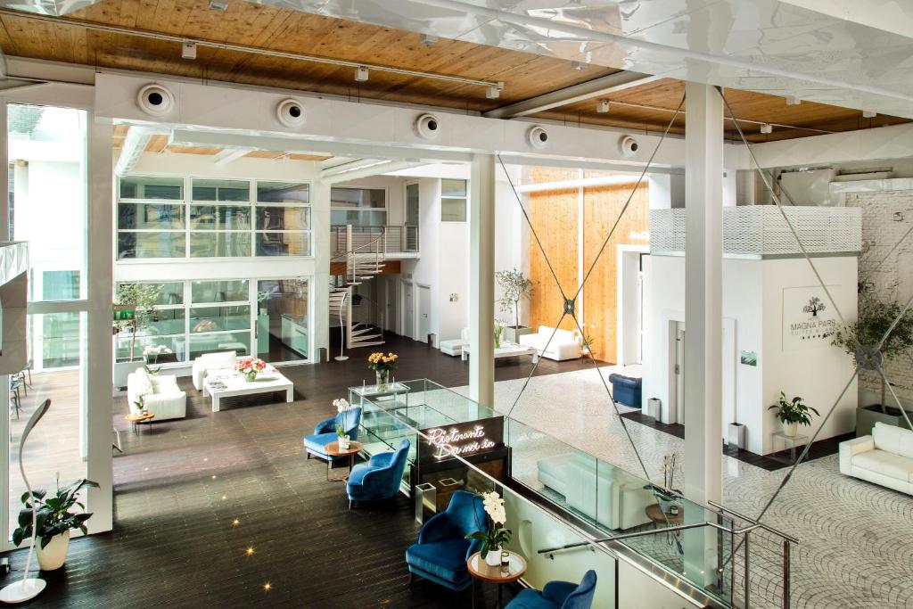 Sala de estar com vários sofás, poltronas e mesas, paredes de vidro e cores claras no Magna Pars l'Hotel à Parfum