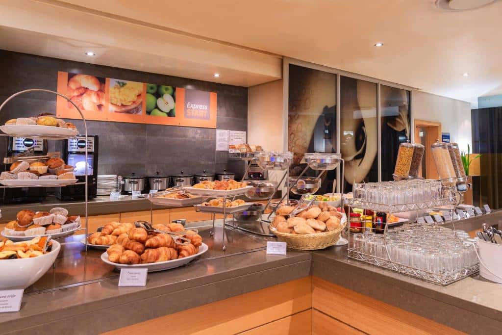 Buffet de pequeno-almoço no Holiday Inn Express com bolos, pães, cereais, copos e uma máquina de café num balcão.