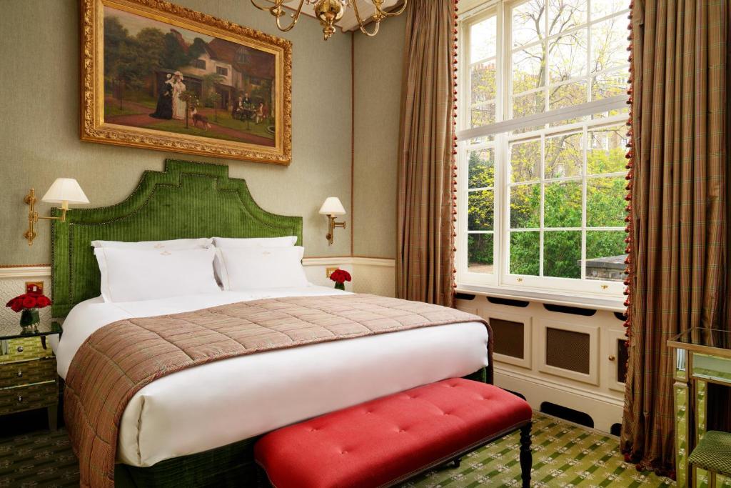 Uma cama bem feita com cabeceira verde, um banco vermelho e uma grande janela num quarto de estilo clássico, no The Montague On The Gardens.