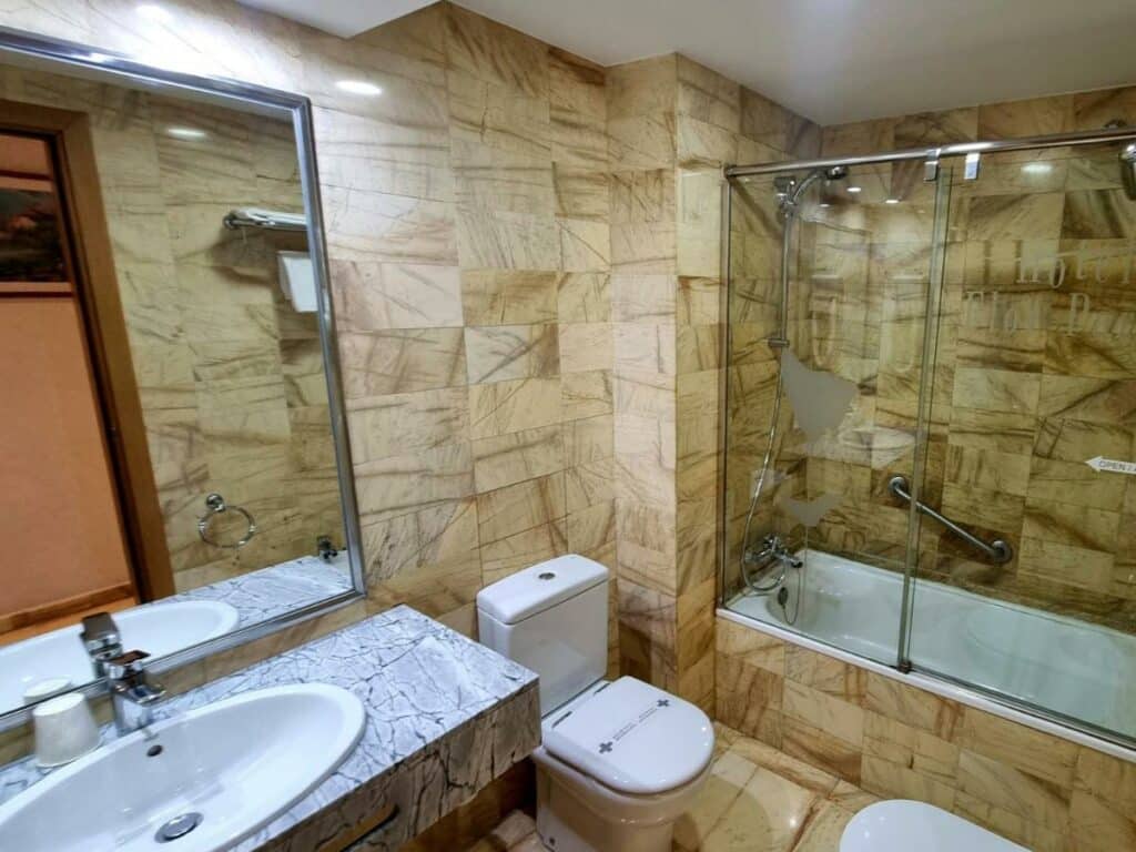 Casa de banho do Flor Parks, com banheira junto à sanita, protegida por uma cabine de vidro, e lavatório com espelho.