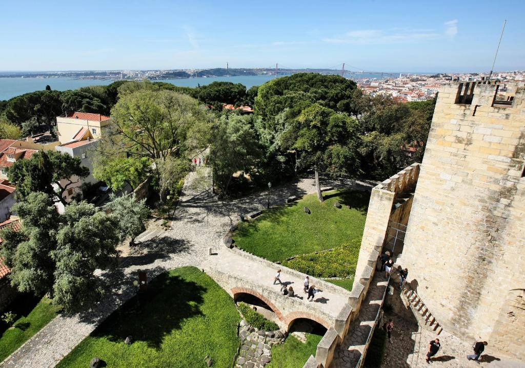 Pátio de um edifício histórico com árvores em redor e vista distante da cidade e do rio sob um céu limpo, onde fica o Solar do Castelo.