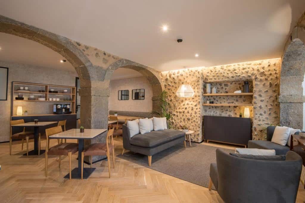 Zona comum do Urbano FLH Hotels Lisboa com sofás, cadeirões e uma televisão, dividida por paredes de betão, com mesinhas quadradas e cadeiras estofadas