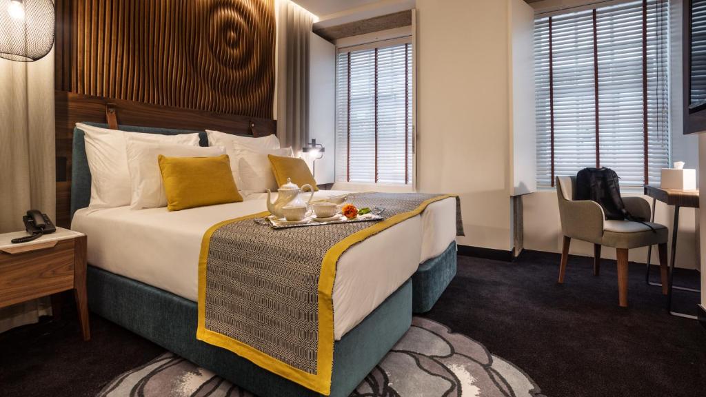 Quarto da Pousada do Porto – Rua das Flores com cama de casal, uma bandeja de pequeno-almoço em cima da cama e, do lado direito, uma cadeira e uma mesa.