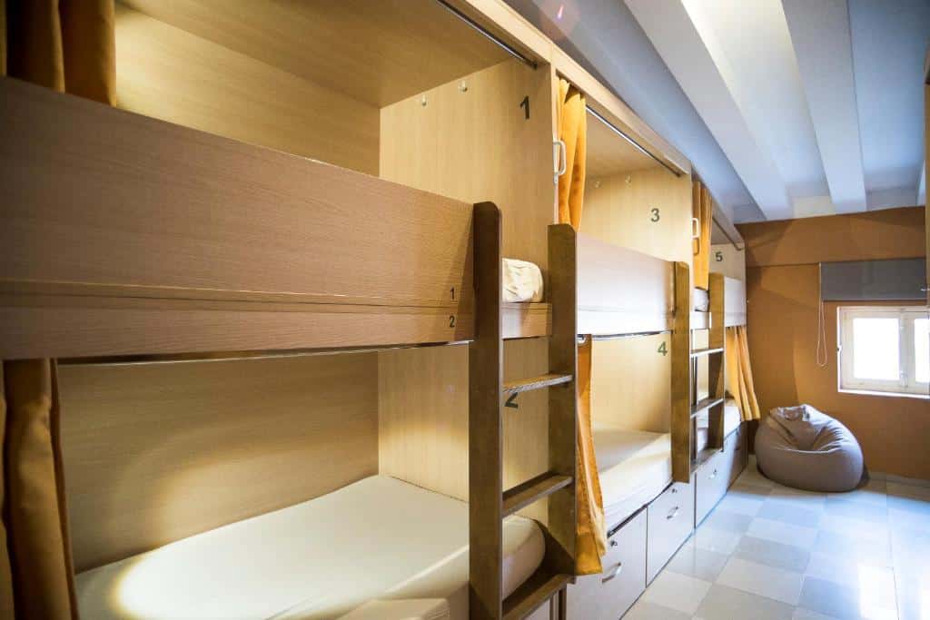 Zona com beliches do River Hostel em design modular, com cama, cómoda e pufe num ambiente acolhedor.