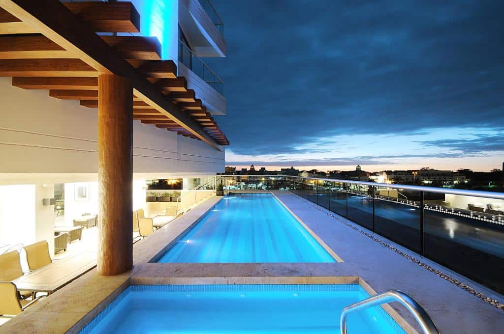 Piscina moderna na cobertura do Holiday Inn Express com iluminação azul, espreguiçadeiras e vista da cidade ao anoitecer.