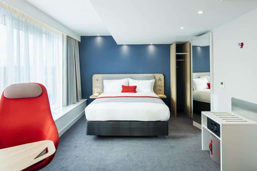 Quarto do Holiday Inn Express Dublin City Centre com paredes azuis, cama branca com almofadas vermelhas e poltrona vermelha.