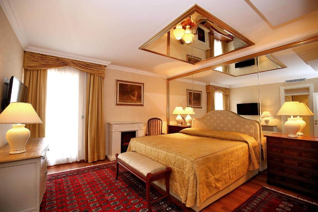 Quarto de hotel luxuoso com cama de casal, espelhos no teto e decoração clássica em tons dourados, no Hotel Niko, em Borik