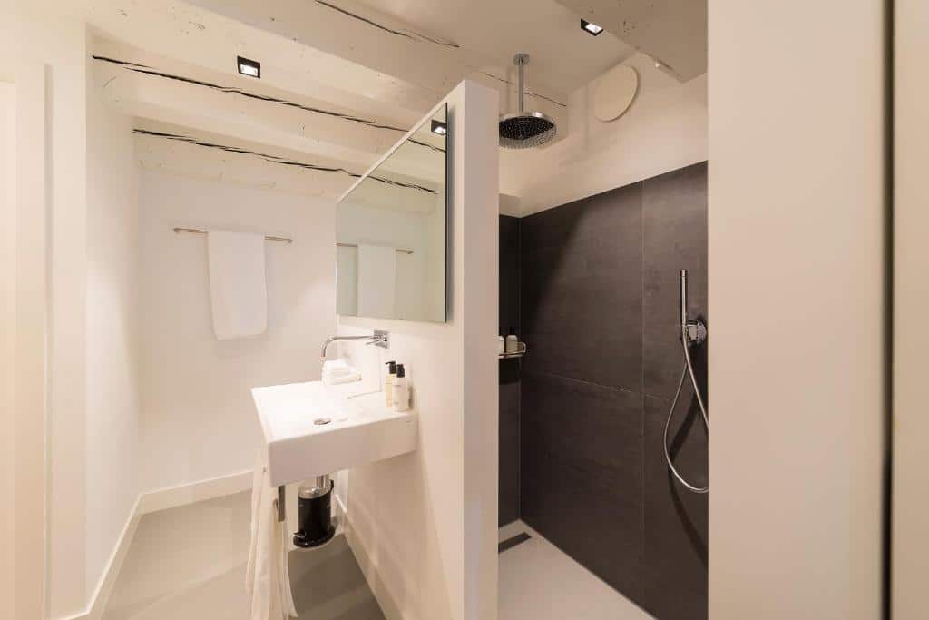 Casa de banho moderna do Milkhouse Luxury Stay Amsterdam, com lavatório branco, espelho, toalheiro e chuveiro com azulejos escuros e efeito de chuva.