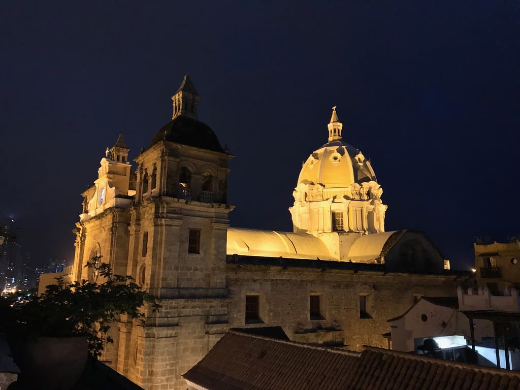 Igreja de São Pedro Claver, em Cartagena, iluminada à noite, com duas torres com campanários e uma cúpula central de estilo colonial.