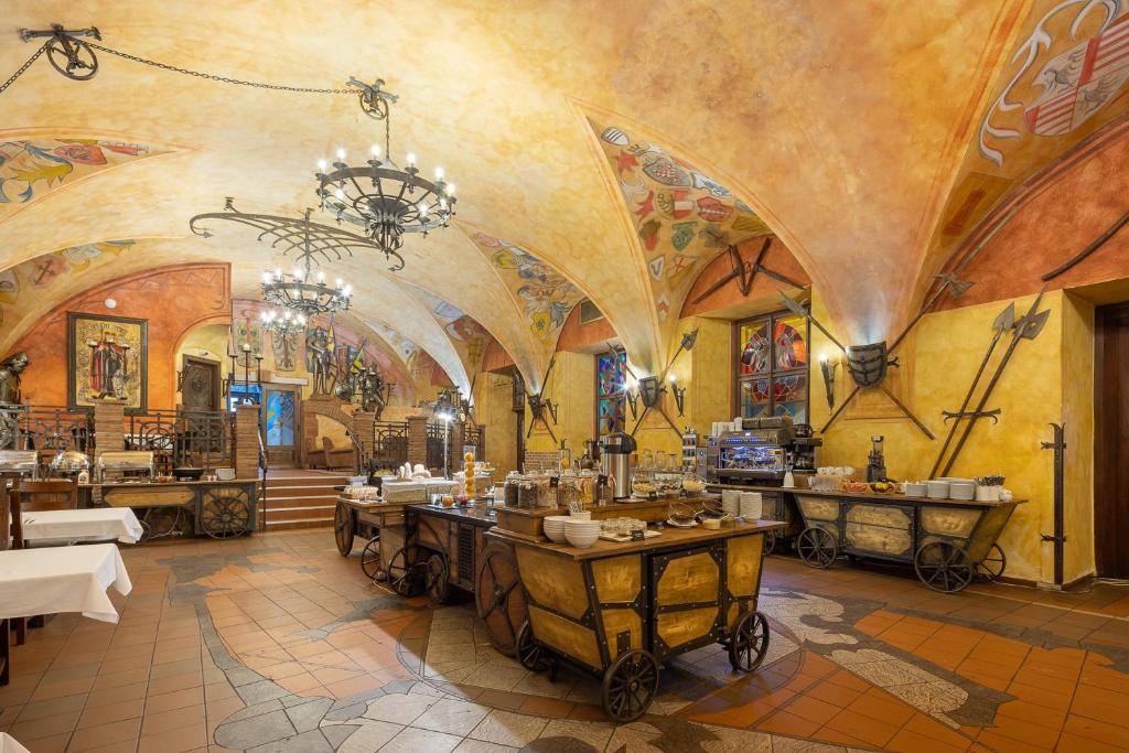 Sala de refeições em estilo medieval do Pytloun Old Armoury Hotel Prague, com tetos em arco, decorações com armas, lustres e mesas de buffet.