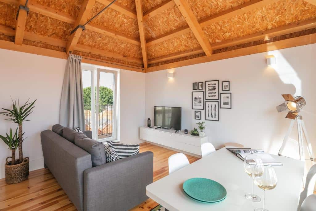 Sala de estar do Indulge Porto Flats, com mesa e quatro cadeiras à direita, sofá à esquerda e um móvel com TV em frente.