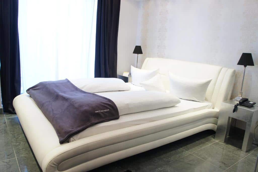 Quarto do Business Wieland Hotel com cama de casal e cómodas com candeeiros dos dois lados. Representa hotéis em Dusseldorf.