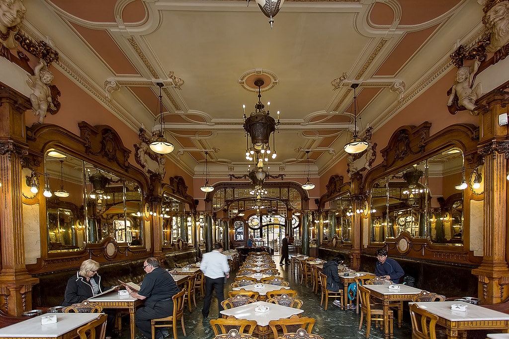 Interior do Café Majestic, com mesas e cadeiras e algumas pessoas sentadas e em pé.