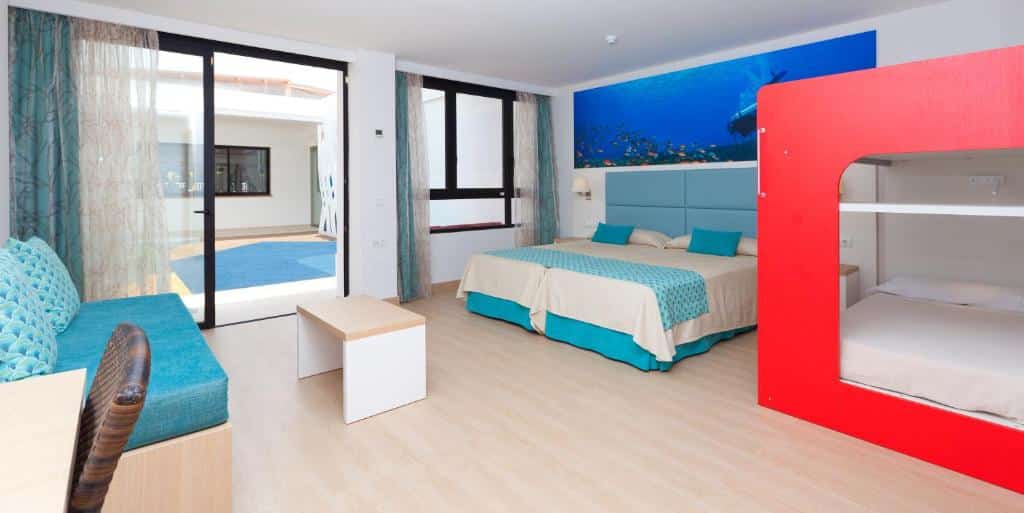 Quarto do Marvell Club Hotel & Apartments com duas camas, um beliche, um sofá, uma secretária e janelas grandes com vista para a zona da piscina.