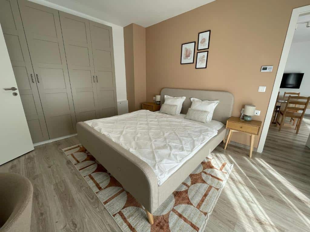 Uma cama de casal do MT Suites ApartHotel bem arrumada, num quarto moderno com paredes bege, duas mesas de cabeceira e um grande roupeiro.