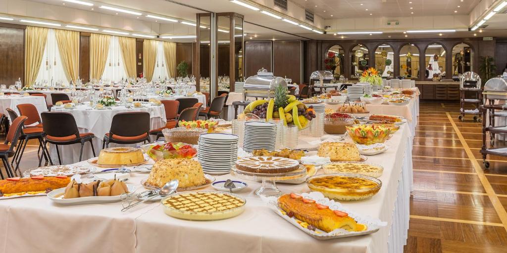 Uma longa mesa de bufete com sobremesas e fruta variada montada numa sala de banquetes formal com mesas redondas, servida no Hotel Fátima.