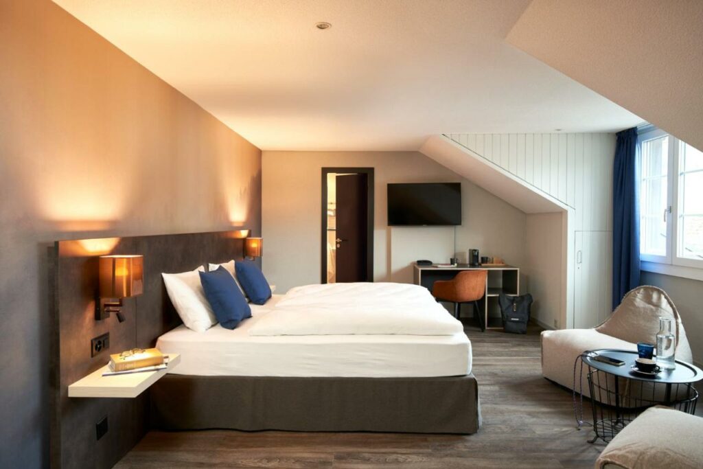 Quarto do The Hey Hotel com cama de casal, secretária e televisão de parede.