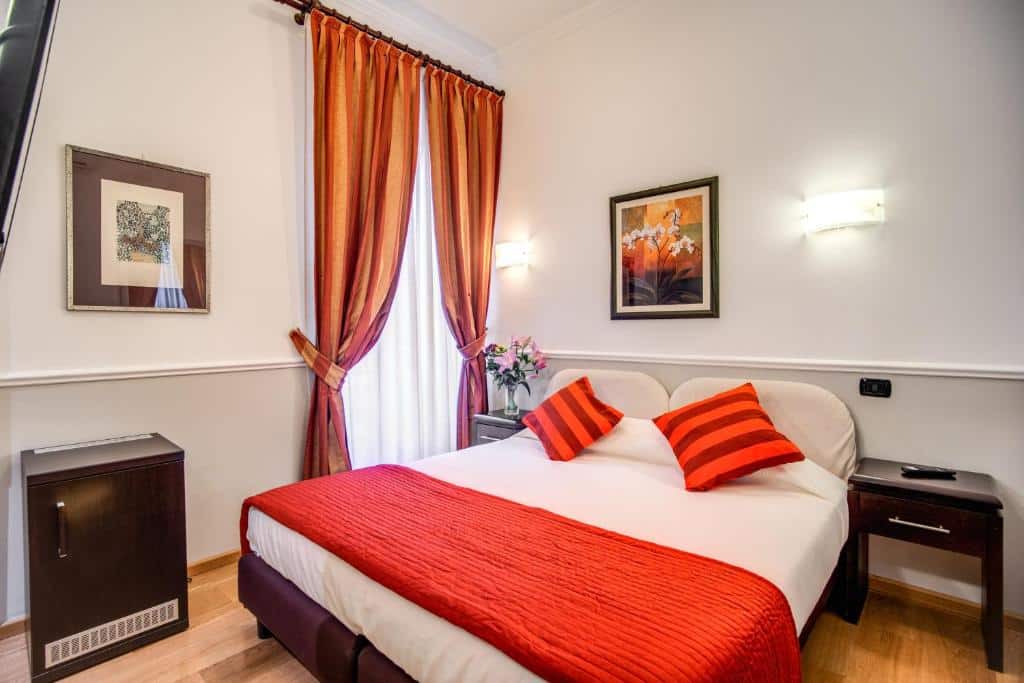 quarto do Hotel Everest Inn Rome, um dos hotéis baratos em Roma, com cama de casal com pormenores laranja a condizer com os cortinados da janela grande, mesas de cabeceira de ambos os lados e uma pequena cómoda