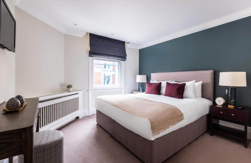 Quarto do Native Mayfair com cama de casal, uma janela com estore, duas mesas de cabeceira, um móvel de madeira com aparador e uma televisão.