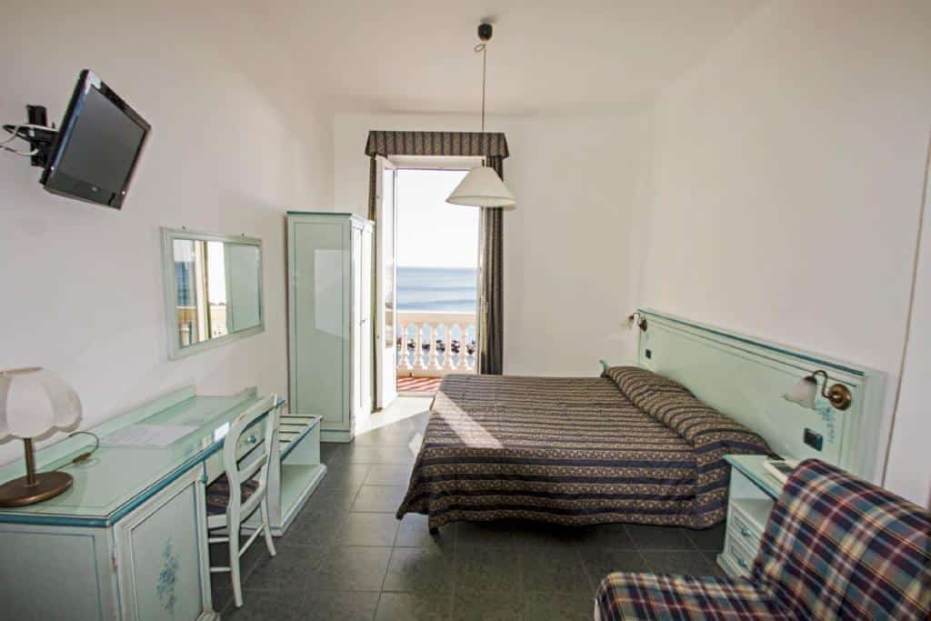 Quarto do Hotel Baia com vista para o mar, decorado em tons pastel com mobiliário vintage e varanda