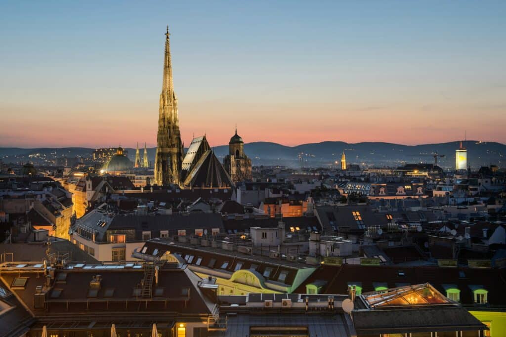 Paisagem urbana de Viena ao pôr do sol, com a Catedral de Santo Estêvão e os telhados, com as montanhas ao fundo.