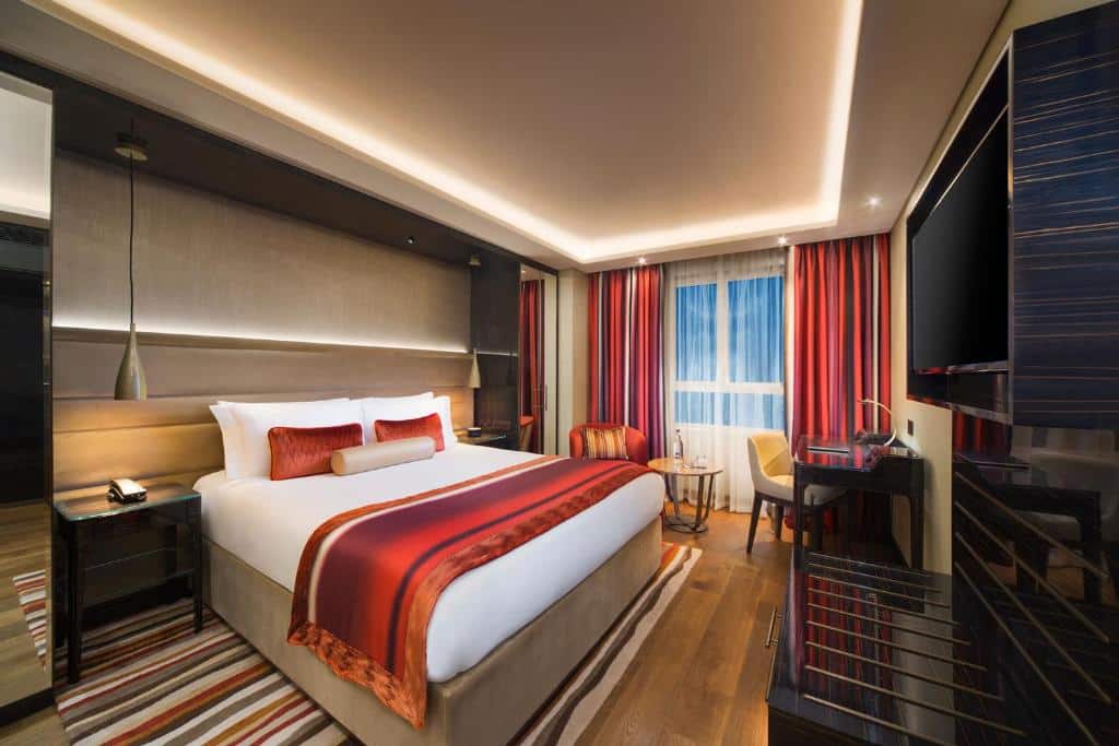 Quarto do The Rathbone Hotel, Fitzrovia com cama de casal, secretária com cadeira, mesa redonda com poltrona, chão em madeira e tapete às riscas