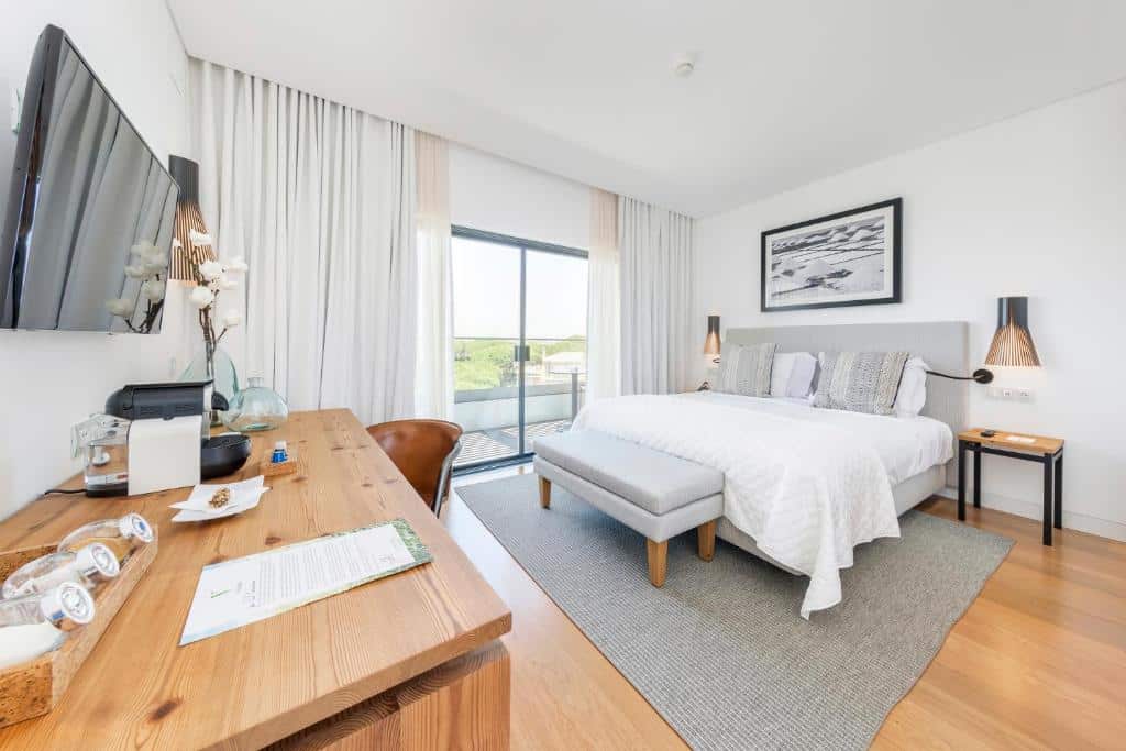 Um quarto moderno no Praia Verde Boutique Hotel, na Praia Verde, com cama de casal, secretária, TV, janela grande e decoração minimalista em tons neutros.