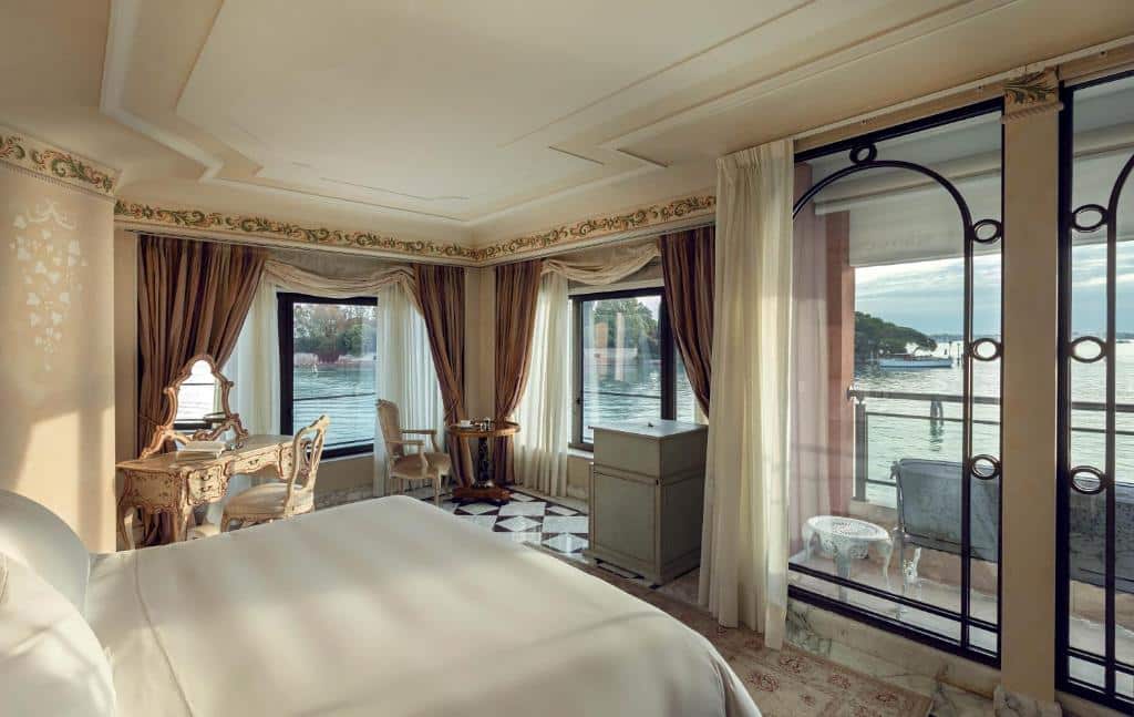 Quarto elegante com vista panorâmica para o mar, decorado com móveis antigos e detalhes dourados, incluindo uma penteadeira entalhada e grandes janelas de vidro